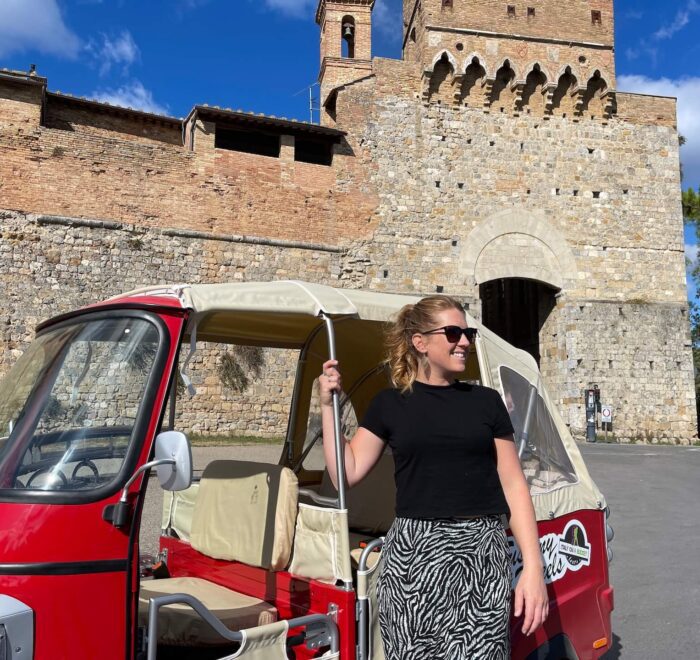 A woman standing next to a red tuk tuk in San Gimignano